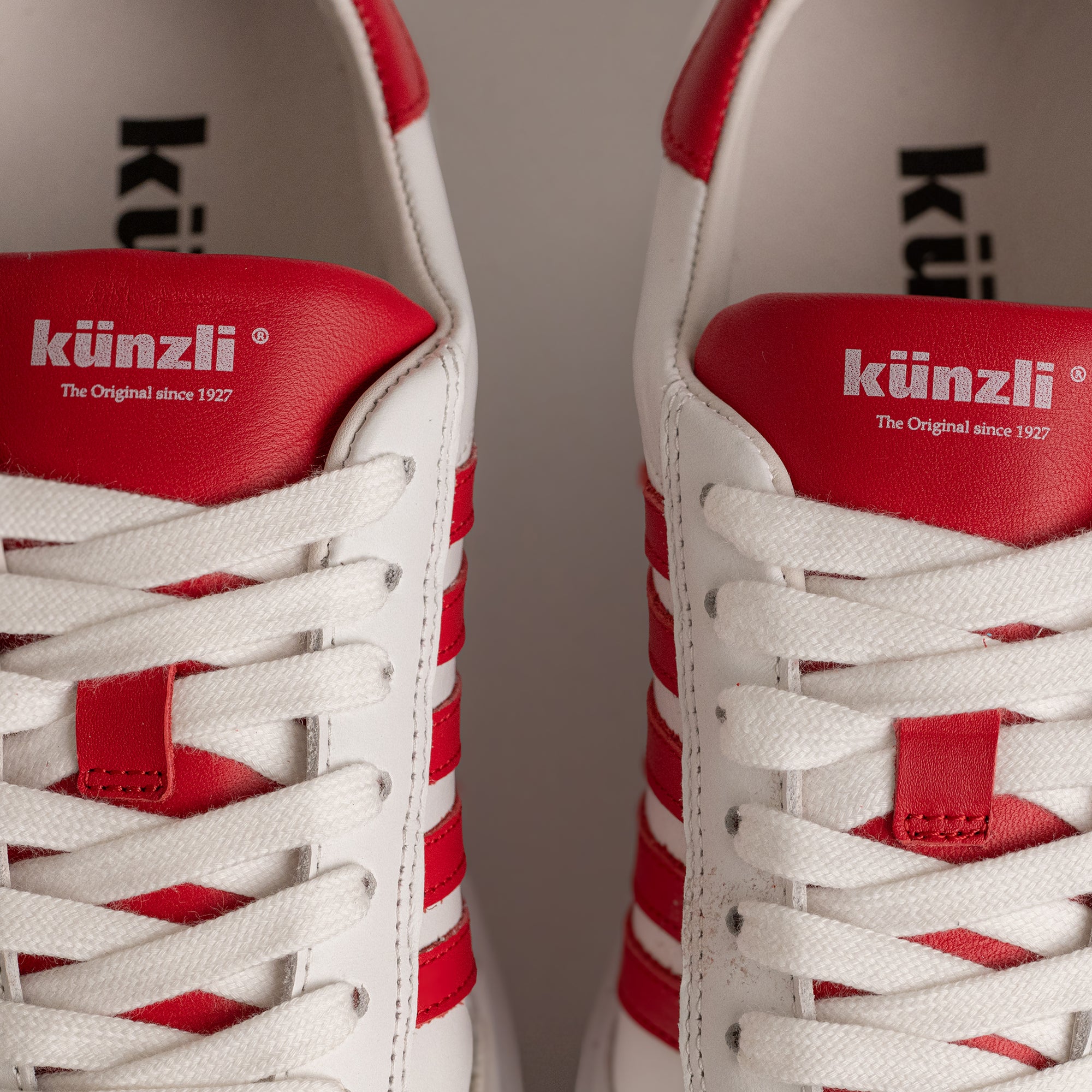 Weiße und rote Kuenzli Schuhe mit Schnürsenkeln, Markenlogo sichtbar auf den Zungen.