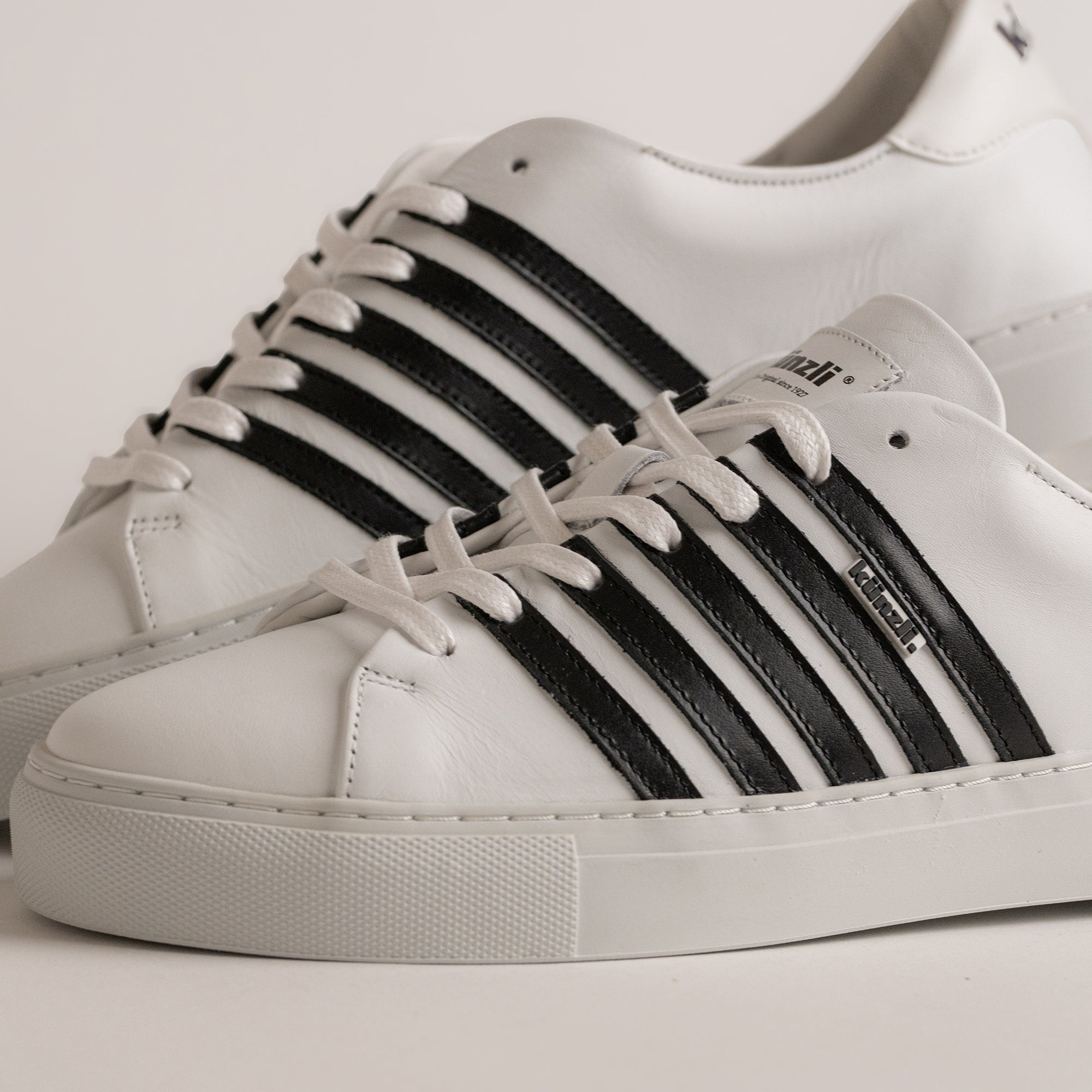Weiße Kuenzli Schuhe mit schwarzen Streifen, aus Leder, auf hellem Hintergrund.