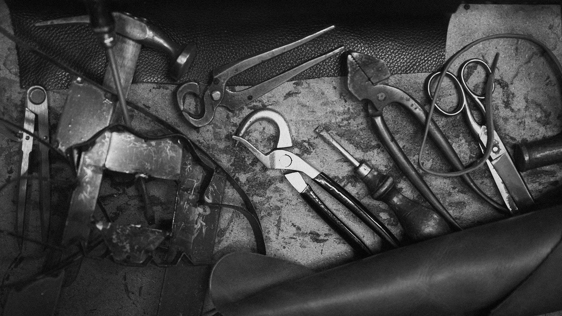 Schuhmacherwerkzeuge auf Lederunterlage, symbolisieren Handwerkskunst von Kuenzli Schuhe.