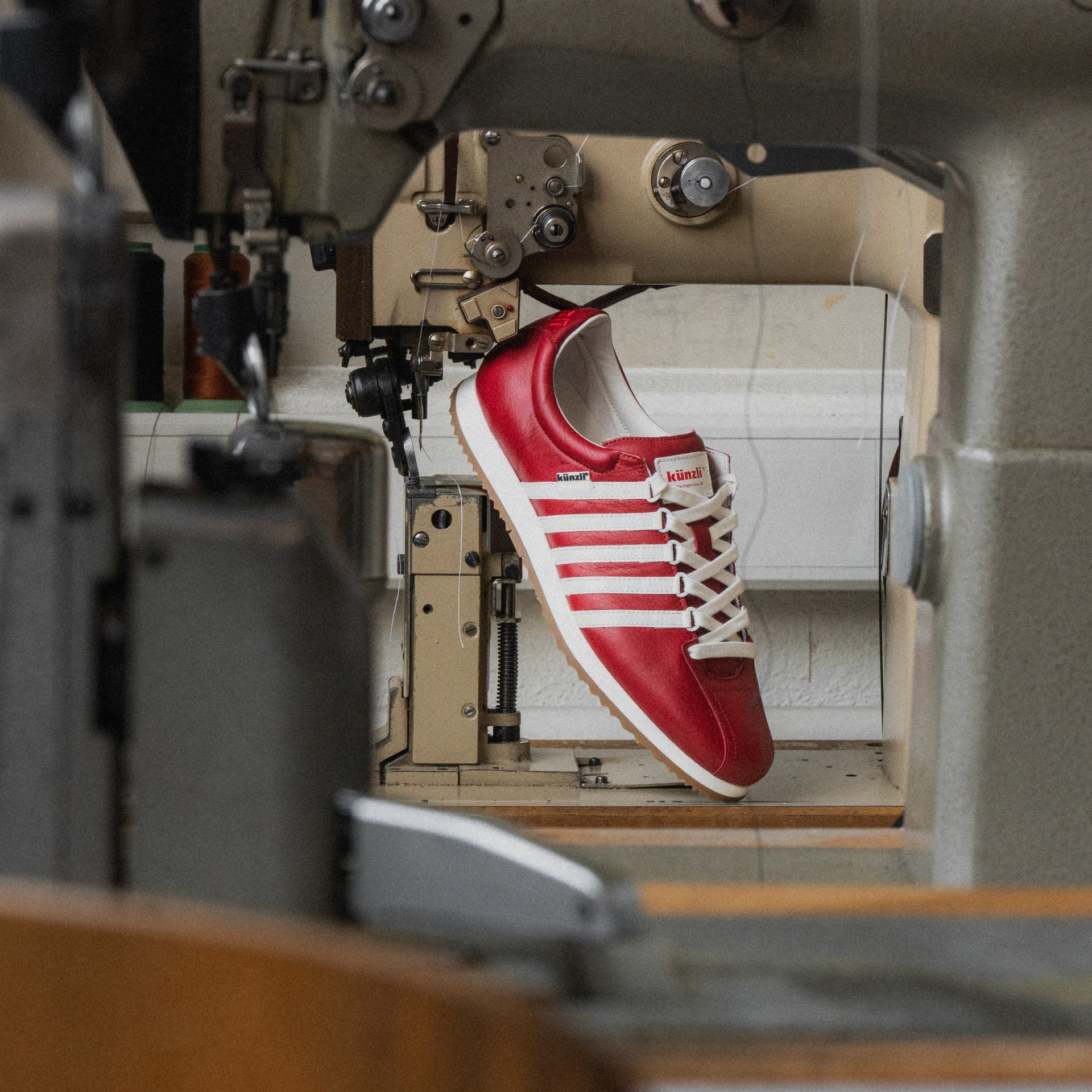 Ein roter Kuenzli Schuh auf einer Nähmaschine in einer Werkstatt.