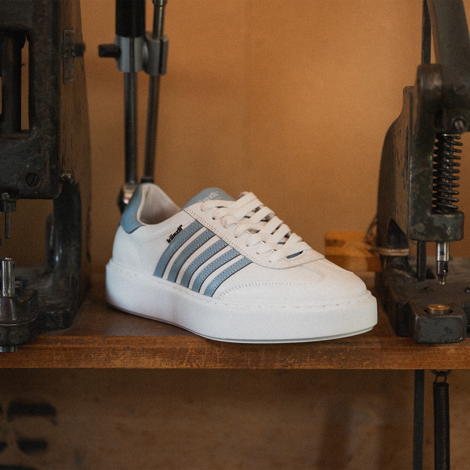 Ein weißer Sneaker von Kuenzli Schuhe mit blauen Streifen auf einem Holztisch.