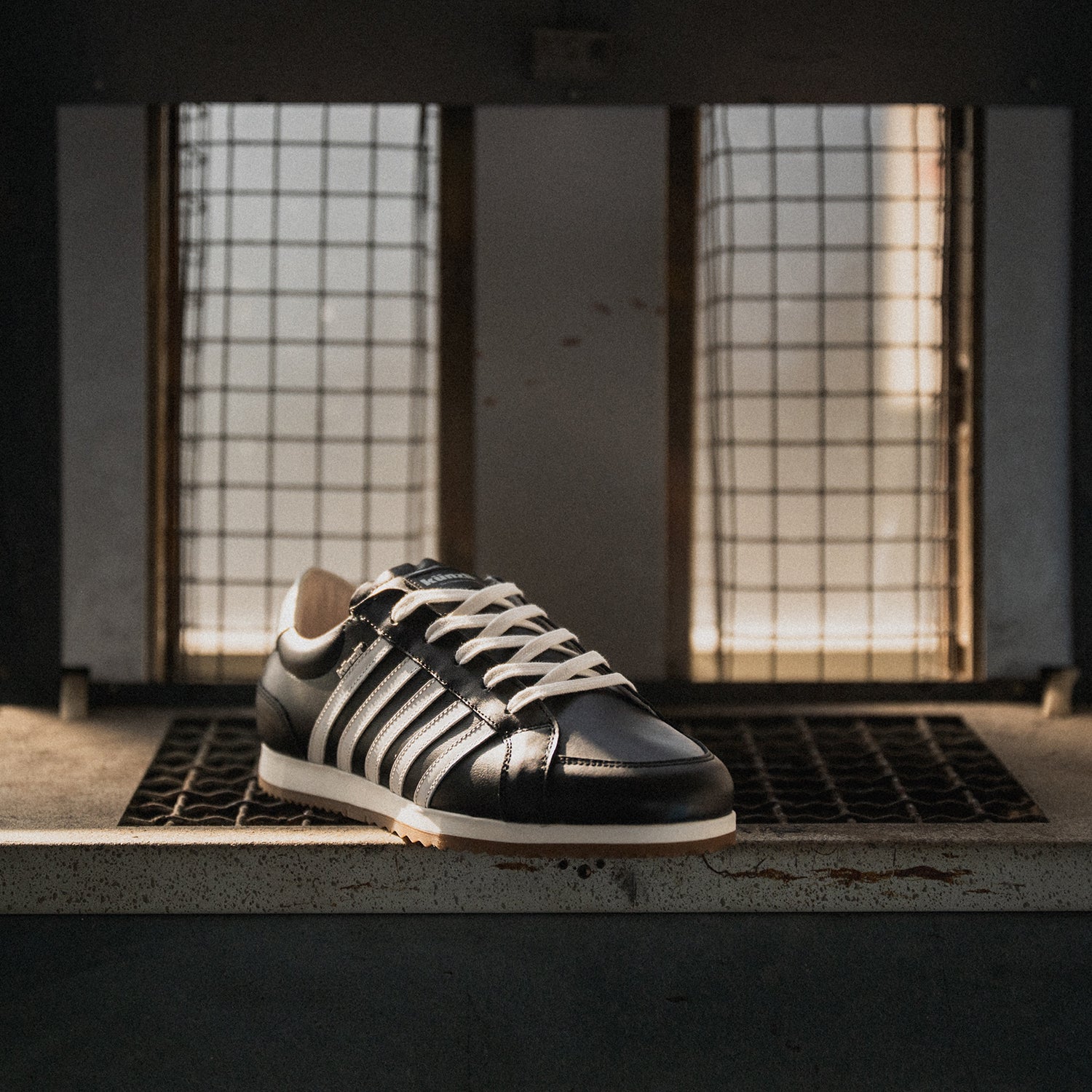 Ein schwarzer Kuenzli Schuh mit weißen Streifen steht auf einem Metallgitter.