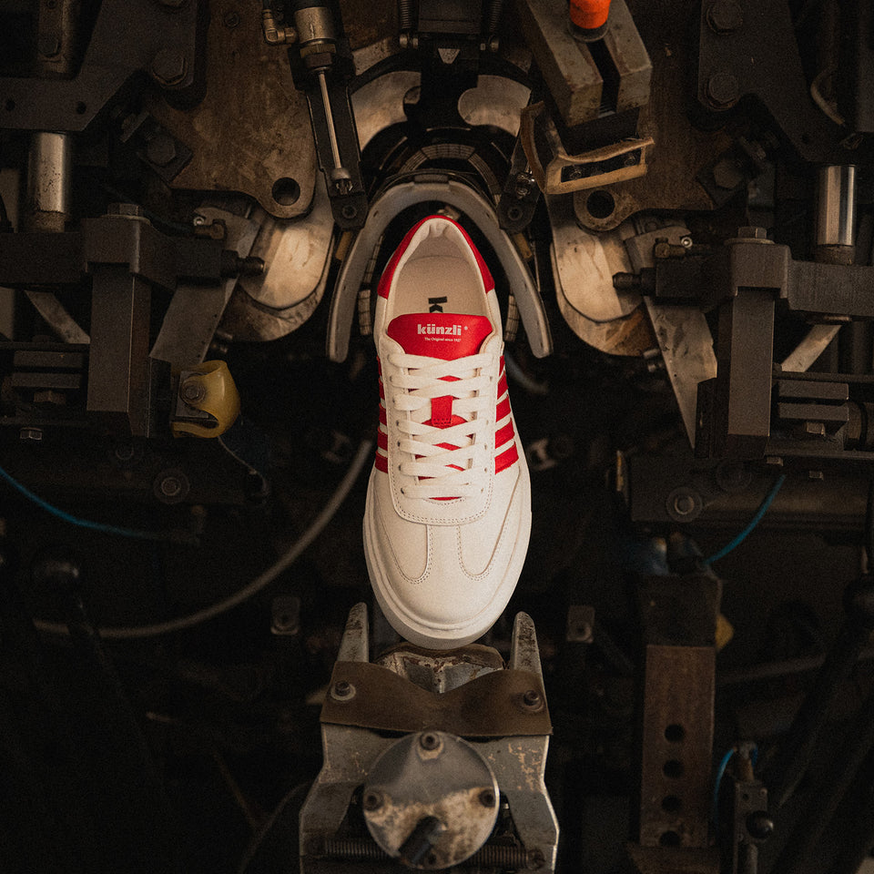 Ein weißer Kuenzli Schuh mit roten Streifen auf industrieller Maschine.