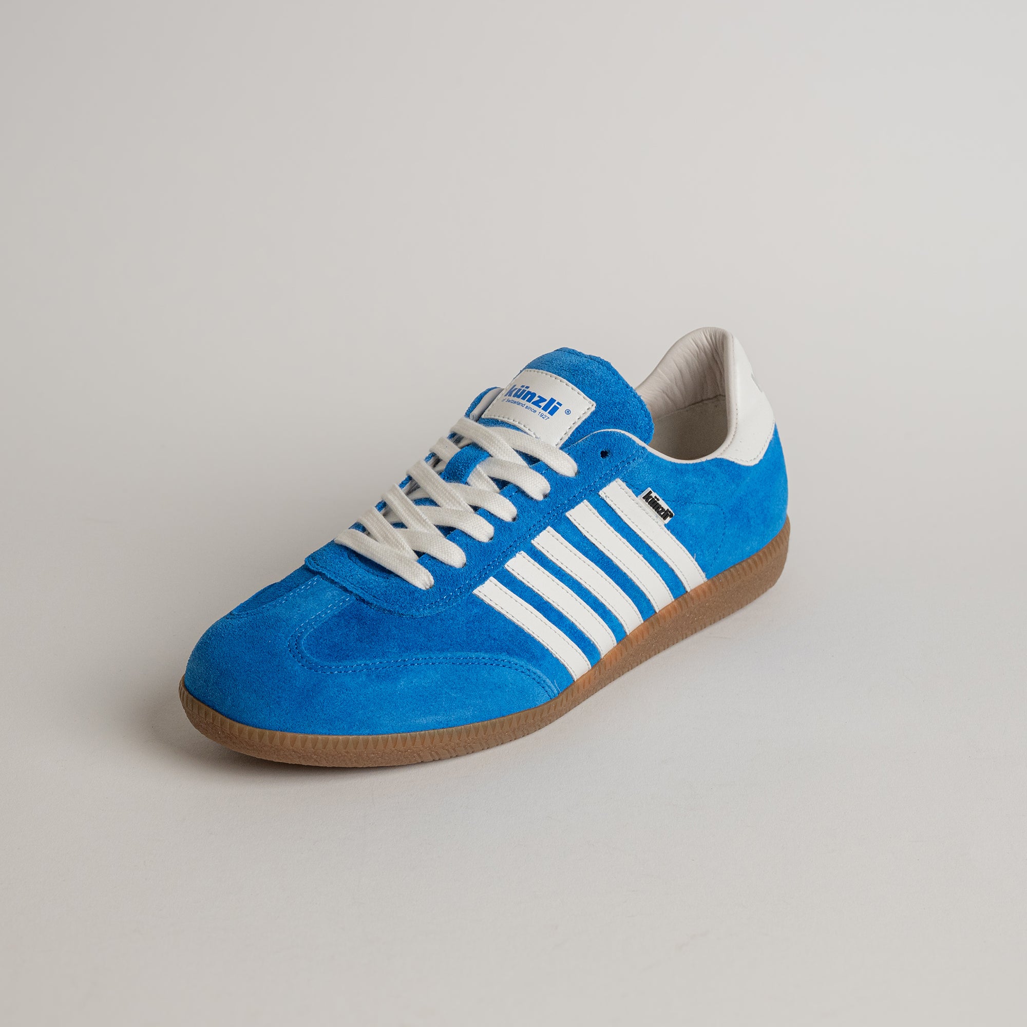 Blauer Kuenzli Schuh aus Wildleder mit weißen Streifen und brauner Sohle.