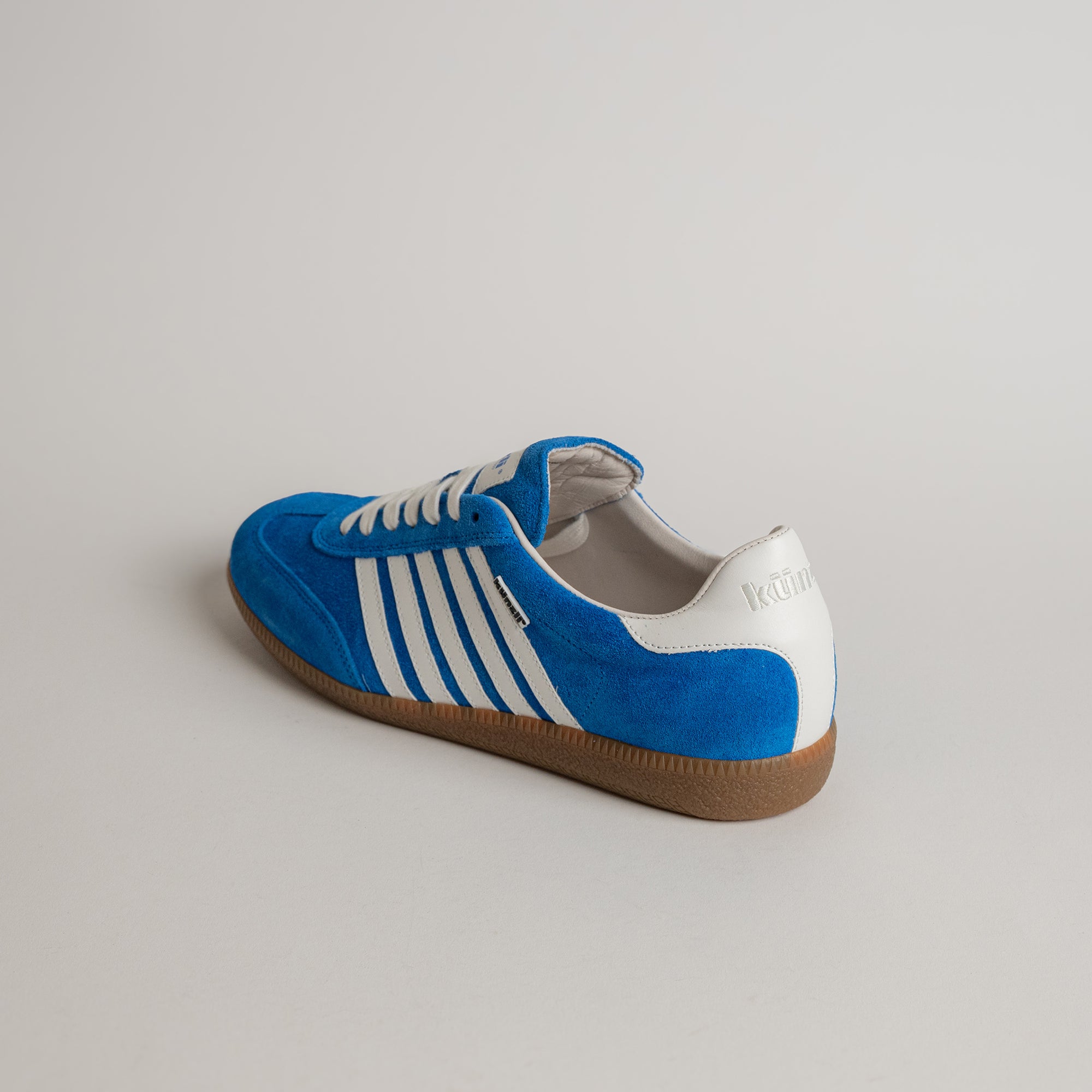 Blauer Kuenzli Schuh aus Wildleder mit weißen Streifen auf hellem Hintergrund.