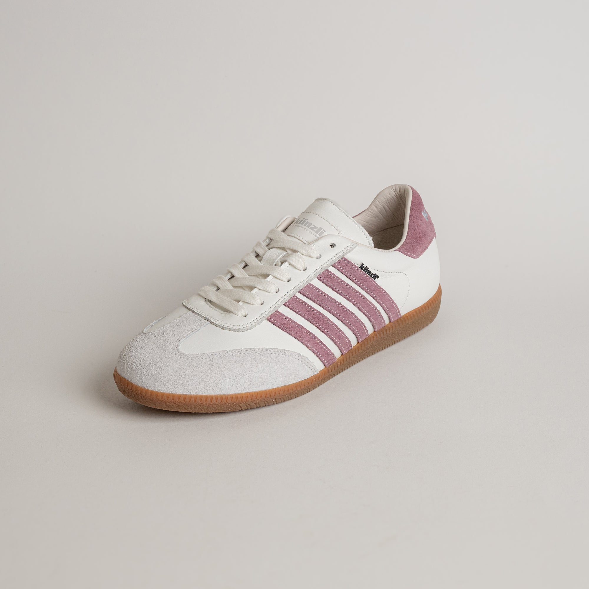 Ein weißer Kuenzli Schuh mit rosa Streifen und brauner Sohle auf hellem Hintergrund.