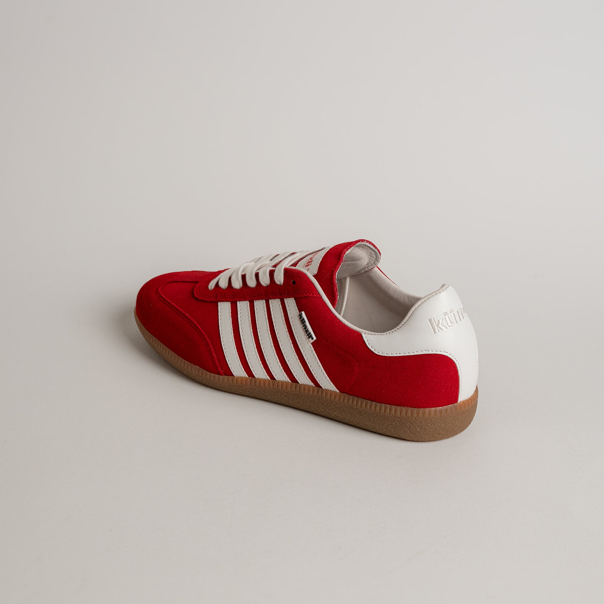 Roter Kuenzli Schuh mit weißen Streifen und Gummisohle auf hellem Hintergrund.