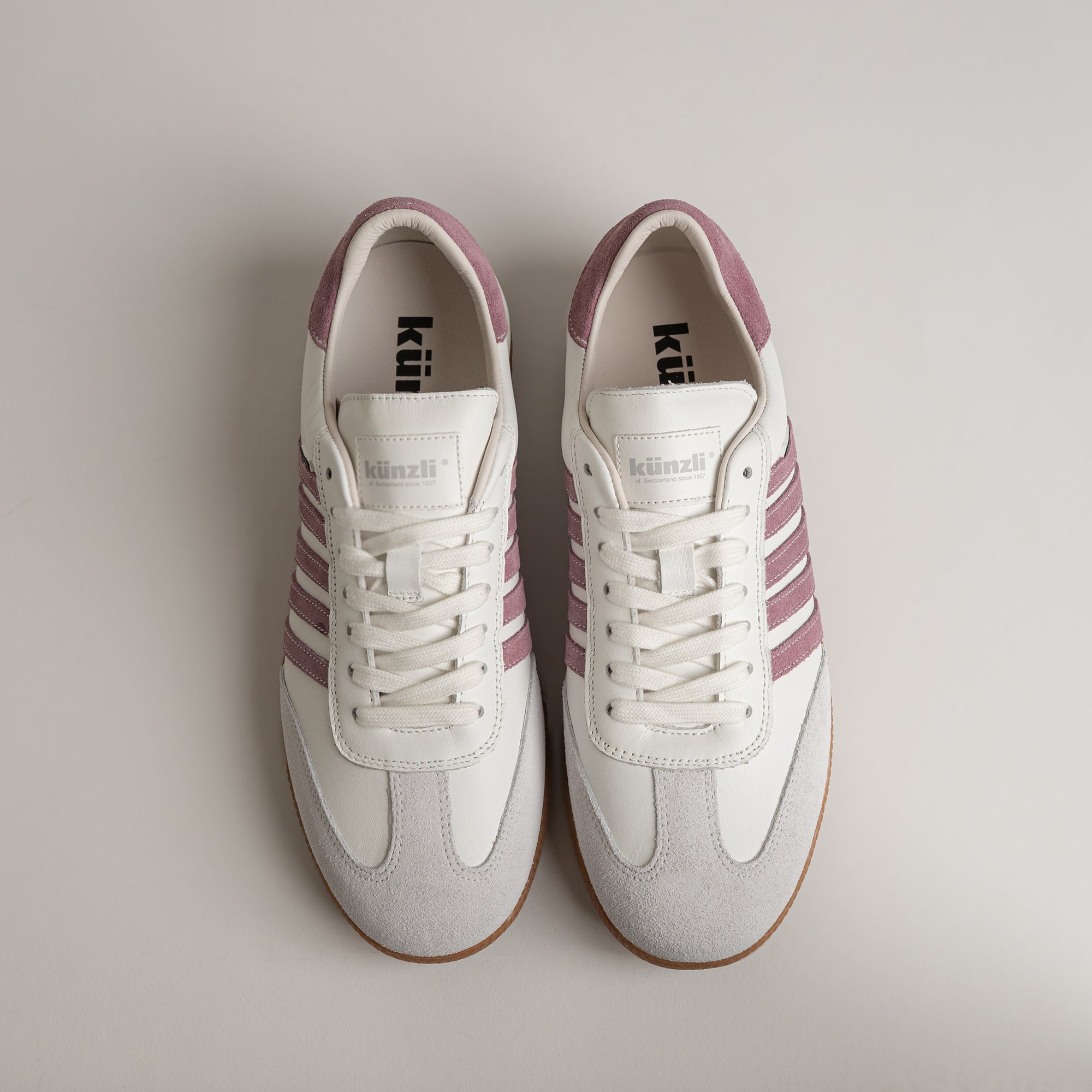 Weiße Kuenzli Schuhe mit lila Streifen auf hellem Hintergrund, sportlich und stilvoll.