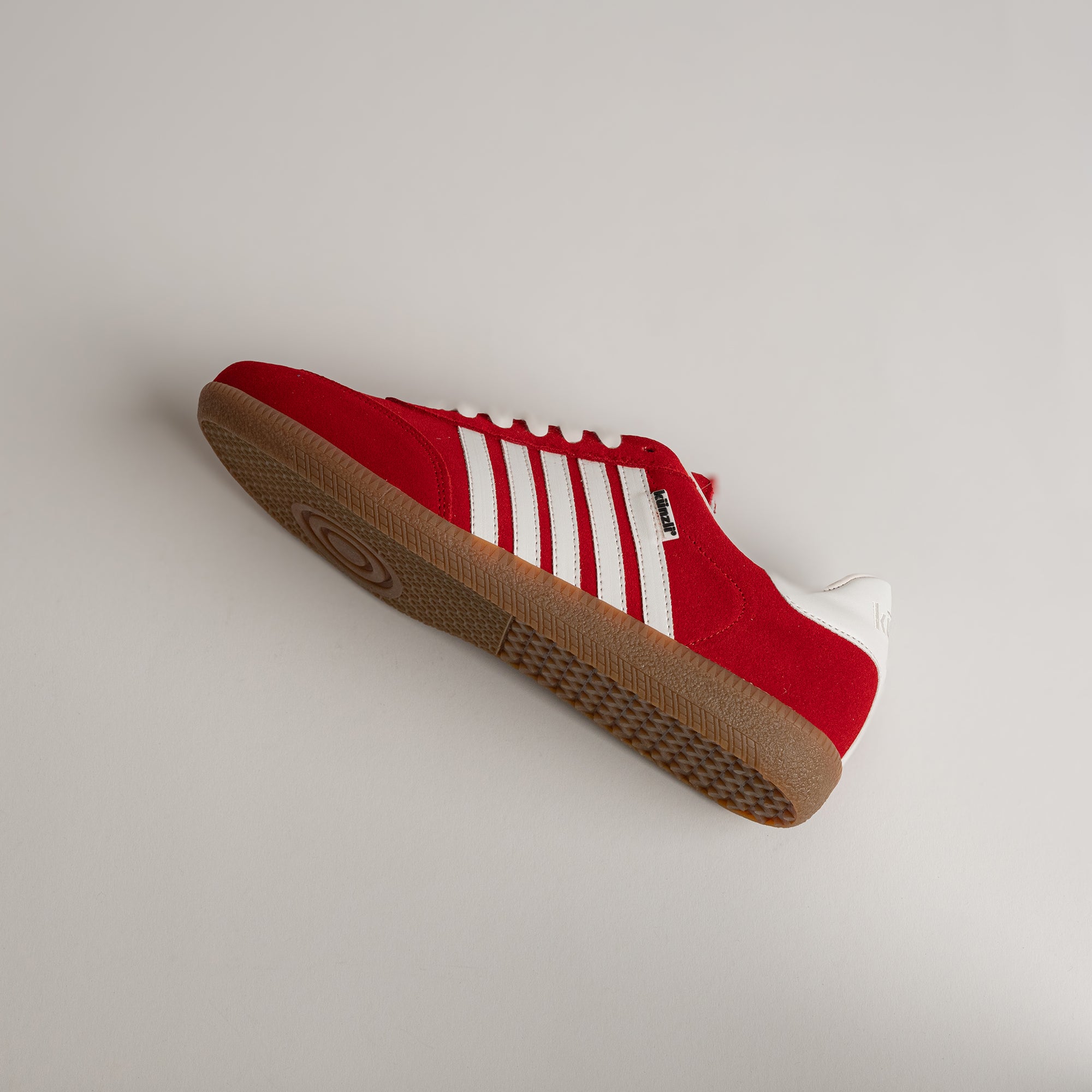 Roter Kuenzli Schuh mit weißen Streifen und Gummisohle auf grauem Hintergrund.