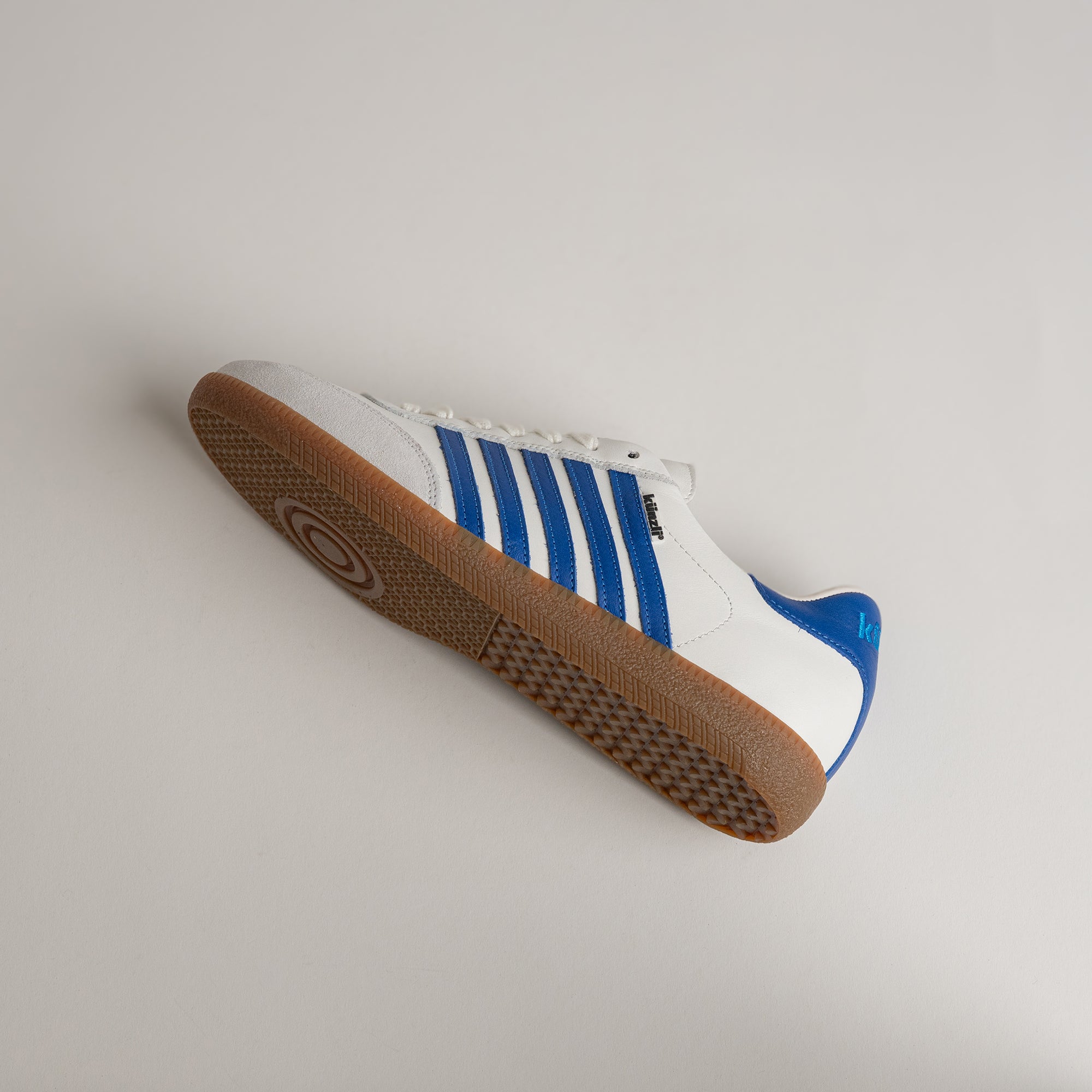 Weißer Kuenzli Schuh mit blauen Streifen und brauner Sohle auf hellem Hintergrund.