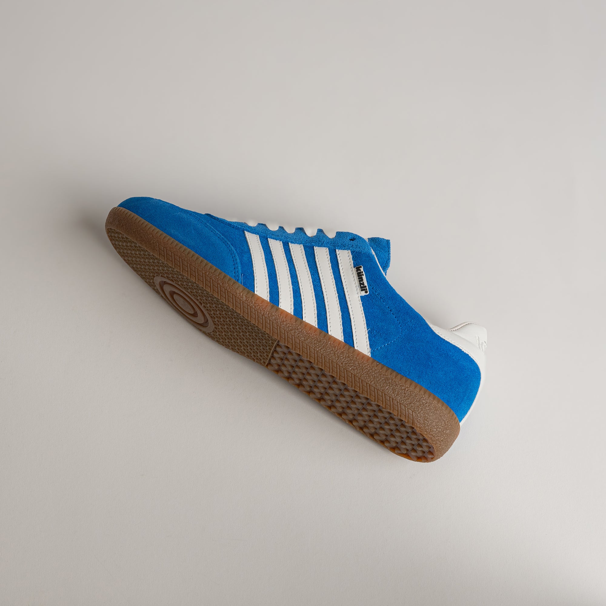 Blauer Kuenzli Schuh mit weißen Streifen und brauner Sohle auf grauem Hintergrund.