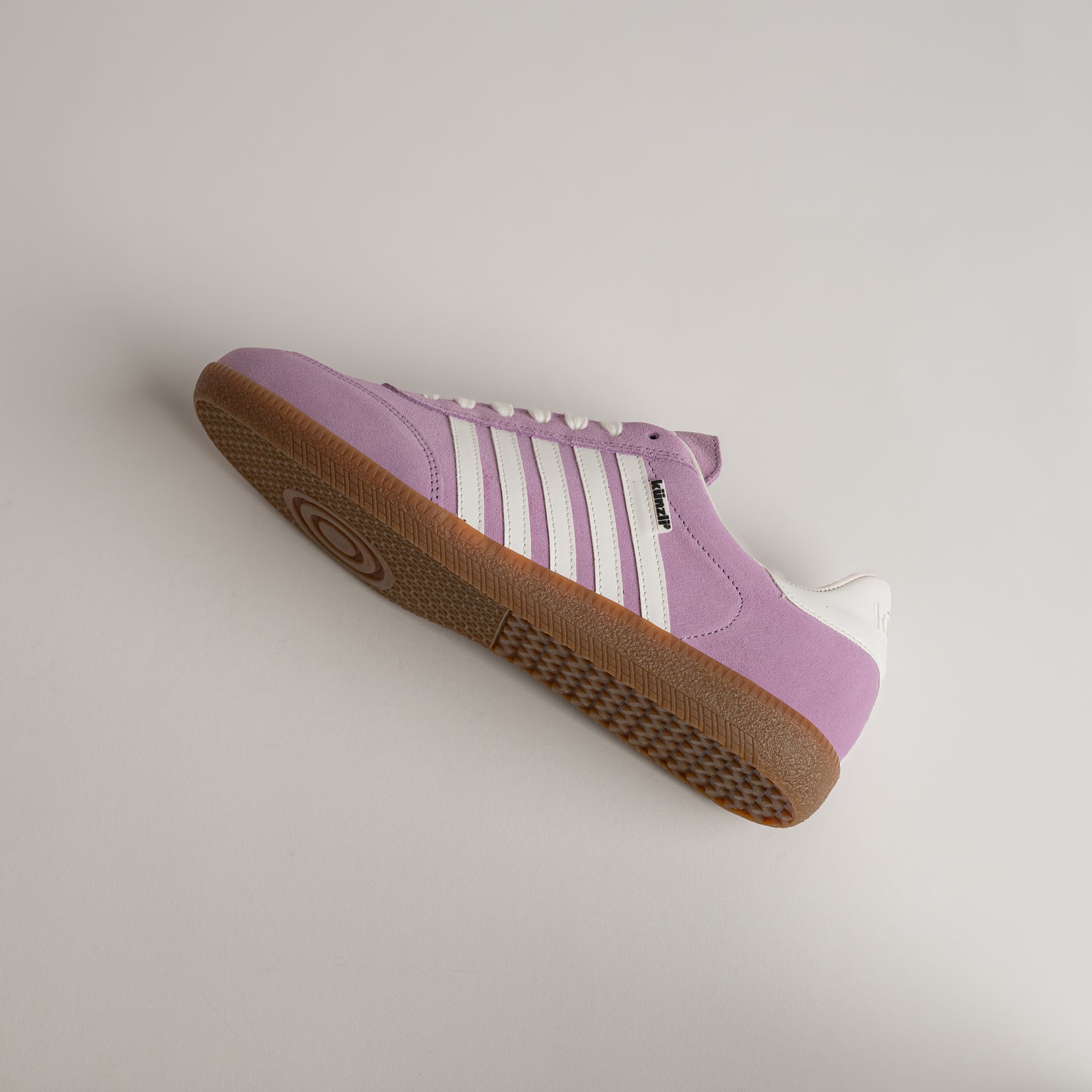 Lila Turnschuh von Kuenzli Schuhe mit weißen Streifen und brauner Sohle.