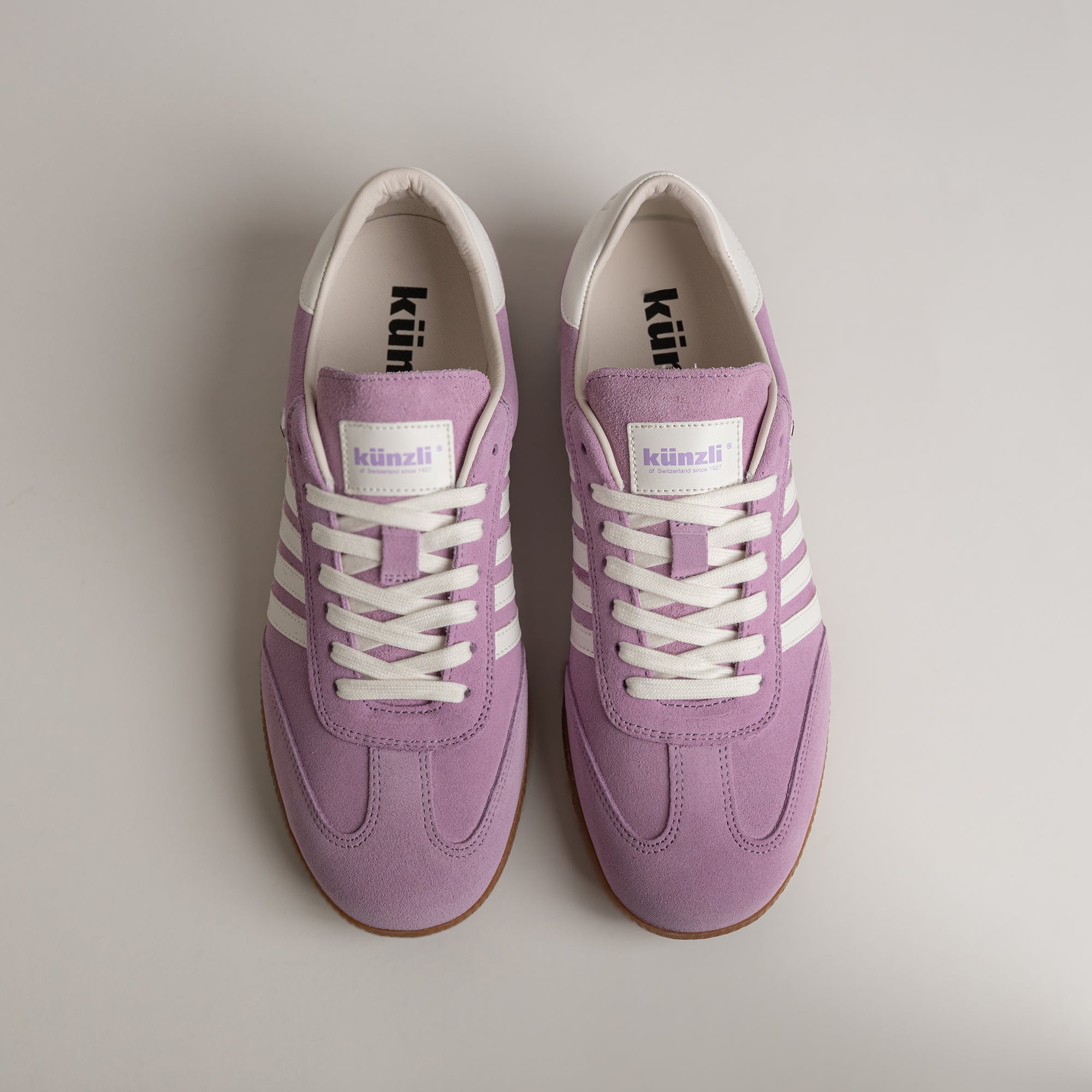 Lila Turnschuhe von Kuenzli Schuhe mit weißen Streifen auf hellem Hintergrund.