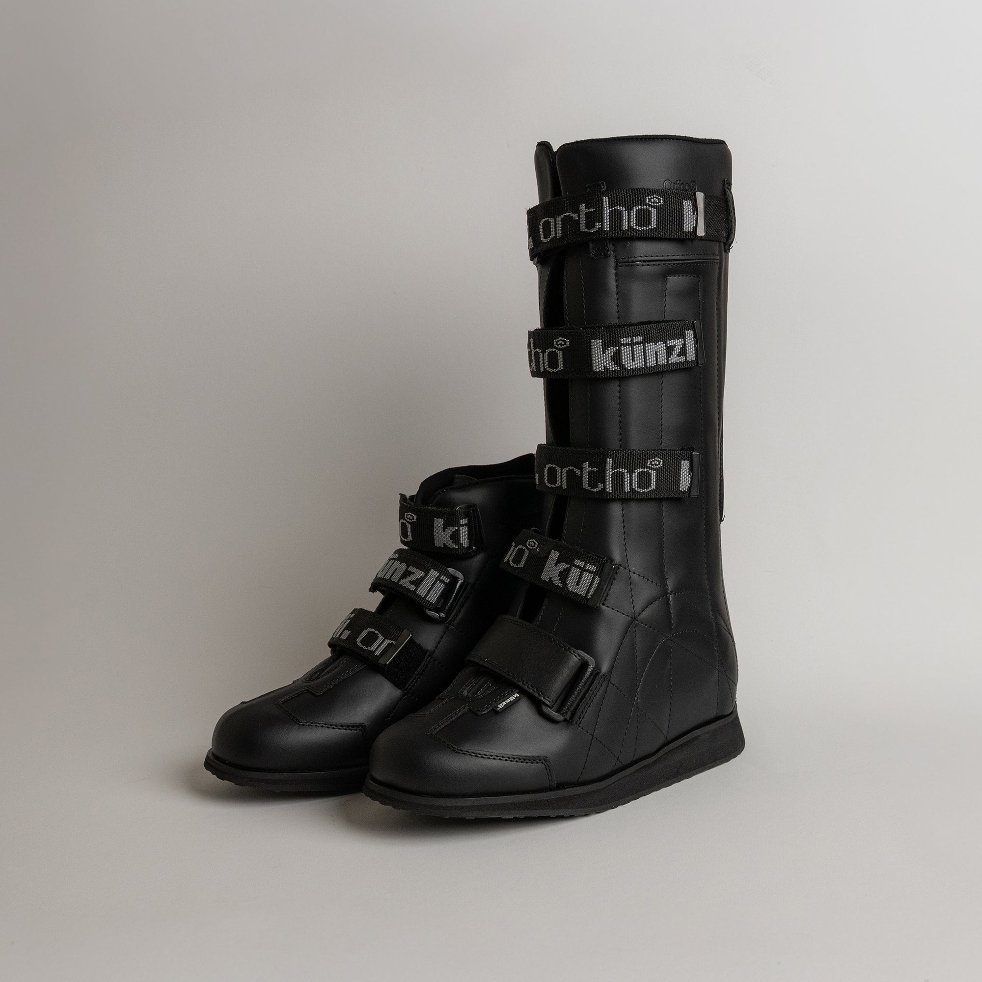 Schwarze orthopädische Stiefel von Kuenzli Schuhe mit Klettverschlüssen auf grauem Hintergrund.