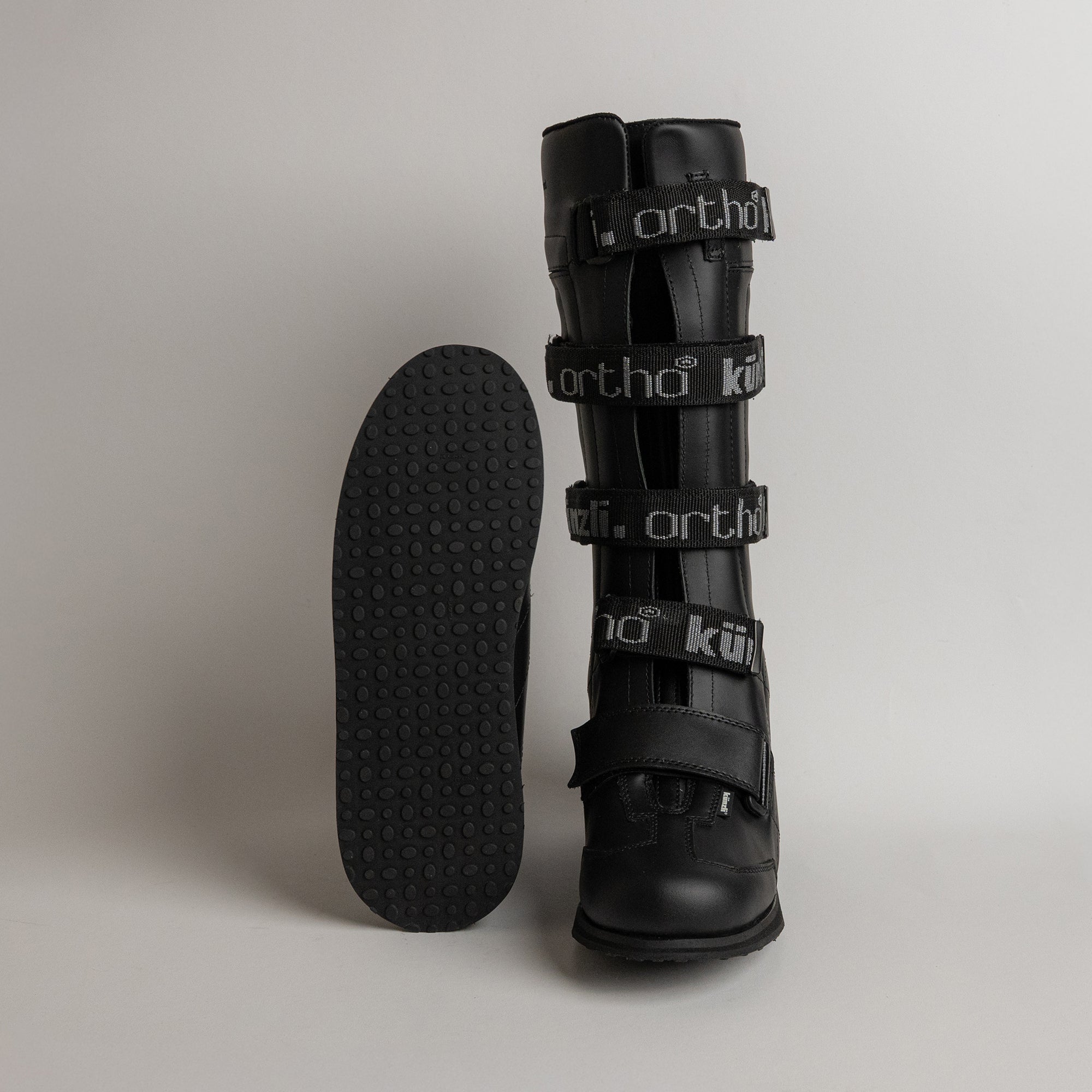 Schwarzer orthopädischer Stiefel von Kuenzli Schuhe mit Klettverschlüssen auf grauem Hintergrund.