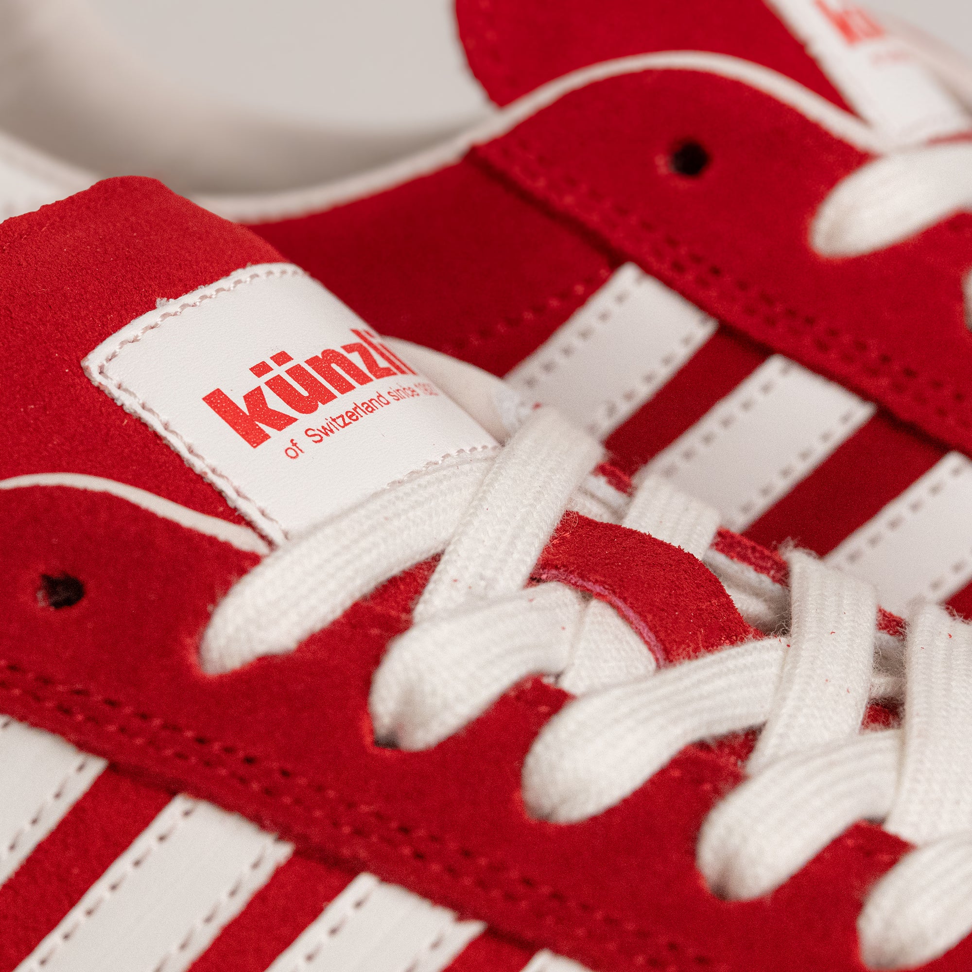 Rote Kuenzli Schuhe aus Wildleder mit weißen Streifen und Schnürsenkeln, Nahaufnahme.