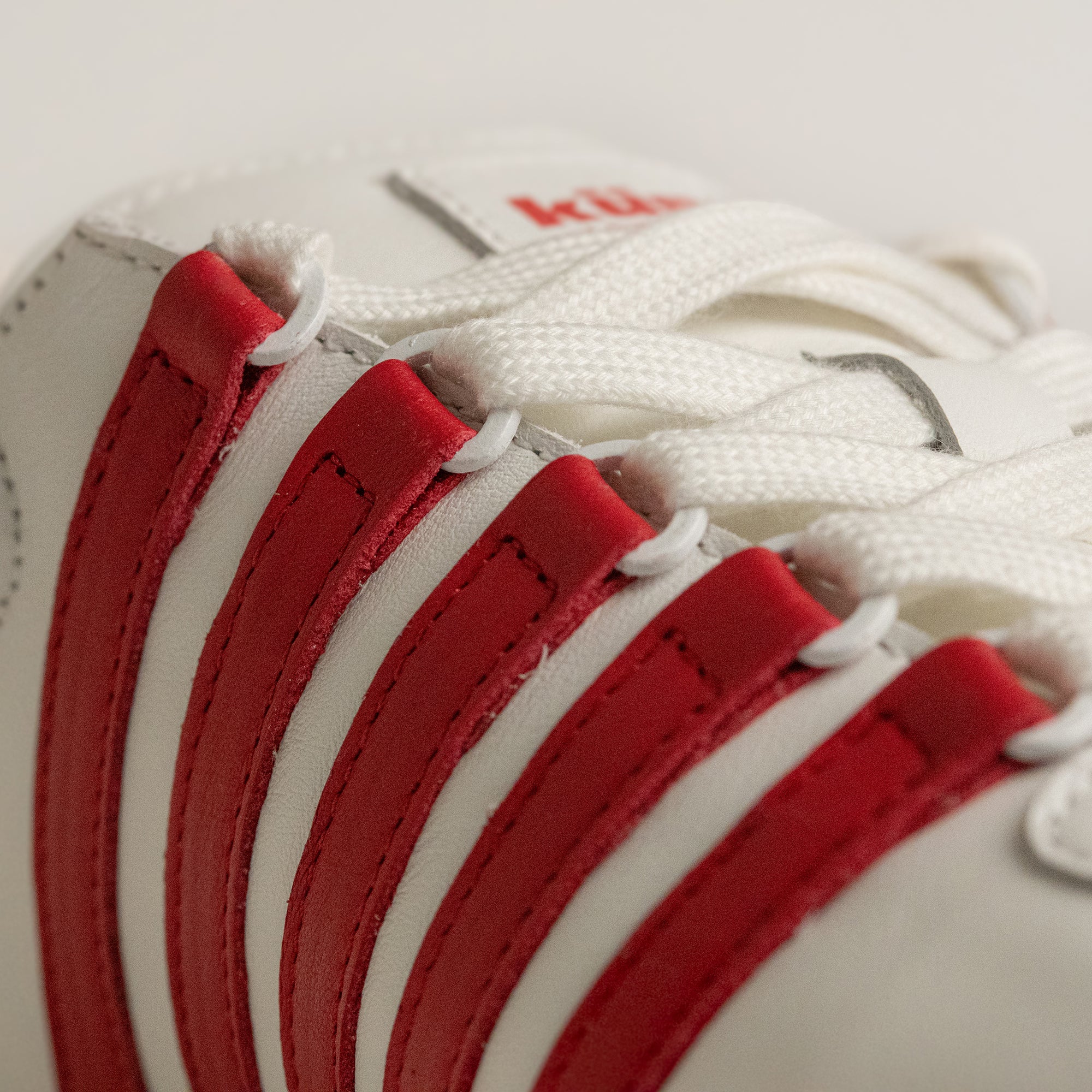 Nahaufnahme eines weißen Kuenzli Schuhs mit roten Streifen und weißen Schnürsenkeln.