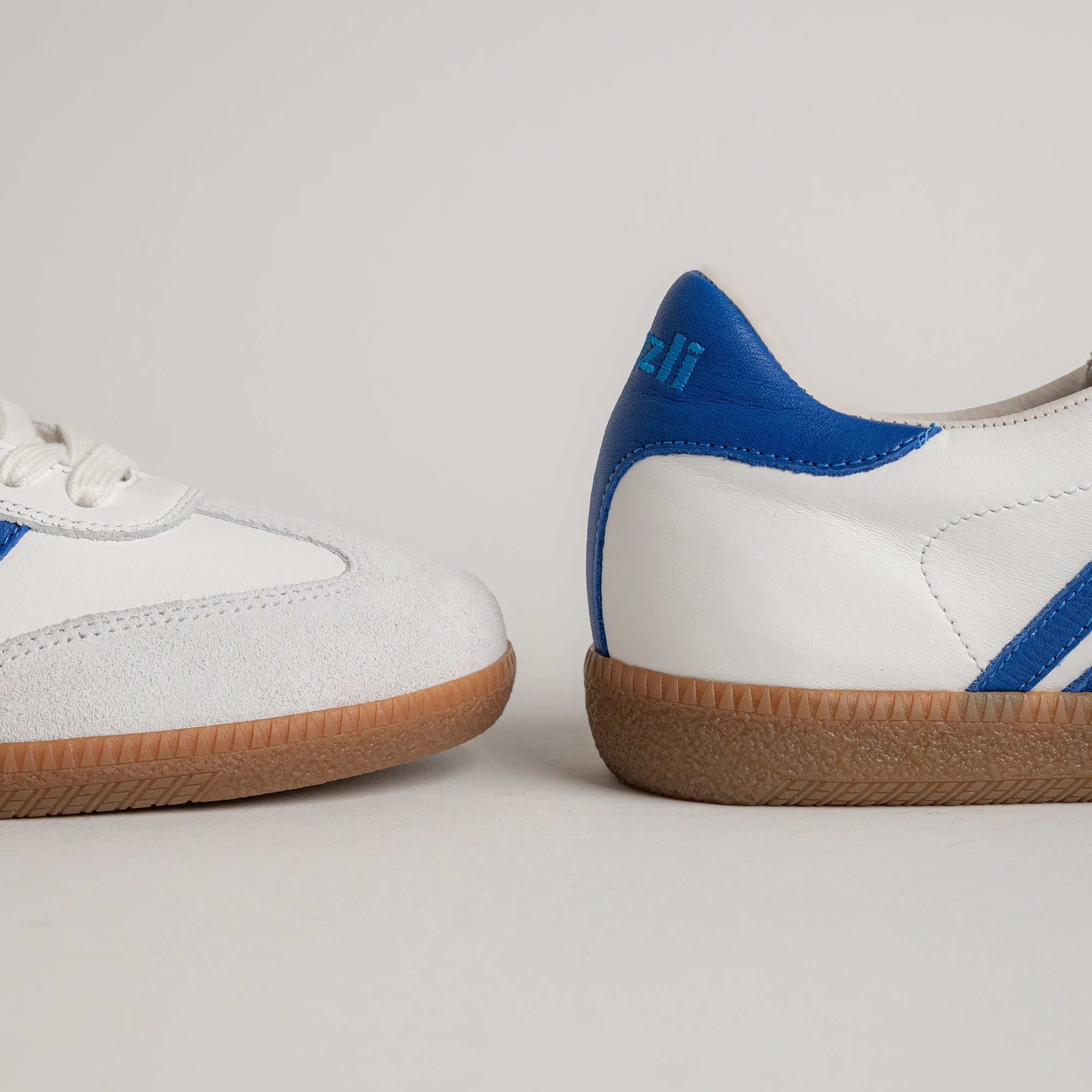 Weiße und blaue Kuenzli Schuhe mit Gummisohle auf grauem Hintergrund.