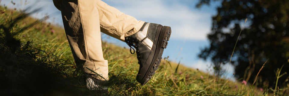 Eine Person trägt Kuenzli Schuhe beim Wandern auf einem grasbewachsenen Hügel.